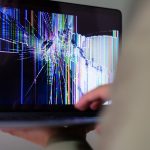 A close-up view of a cracked laptop screen displaying colorful digital distortion.