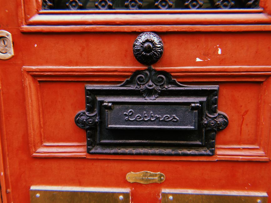 Classic French letterbox on a red wooden door in Paris.
