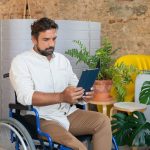 <h1>Federated Adaptive Autonomy: The New Benchmark for Edge and IoT Intelligence</h1> Man in a wheelchair using a tablet in a modern workspace with plants.