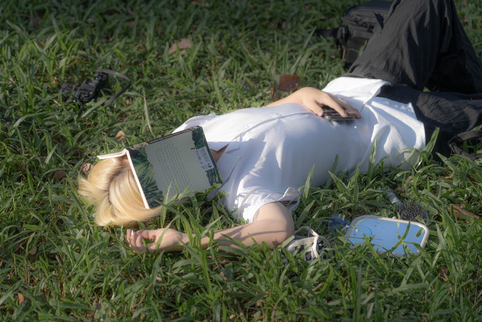 Young adult lies on grass in Hanoi park, book covering face, enjoying a sunny day.