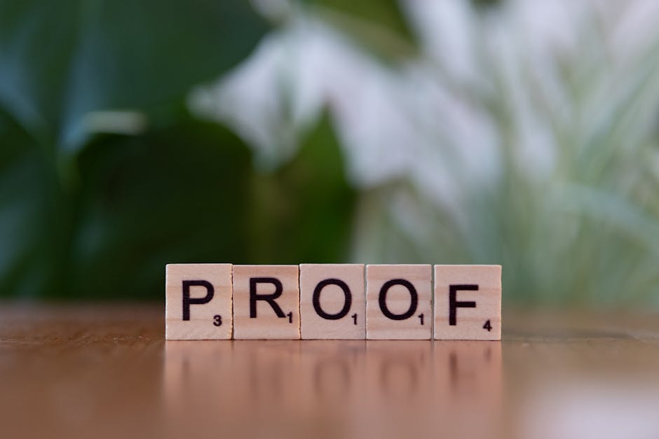 Wooden Scrabble tiles spelling 'PROOF' on a wooden table with green background.