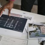 <h1>Graph-Based Connectomics: Architecting the Future of Urban Systems</h1> Architect hands reviewing architectural blueprints and design documents in an office setting.
