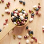 Close-up of assorted beans and legumes on a wooden spoon, showcasing diversity in food ingredients.