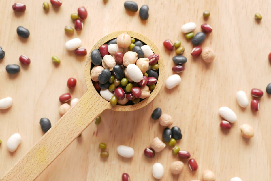 Close-up of assorted beans and legumes on a wooden spoon, showcasing diversity in food ingredients.