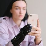 Human-In-The-Loop Adaptive Autonomy: Neuroethical Design Guide A young woman with a prosthetic hand uses a smartphone indoors, symbolizing technology and empowerment.