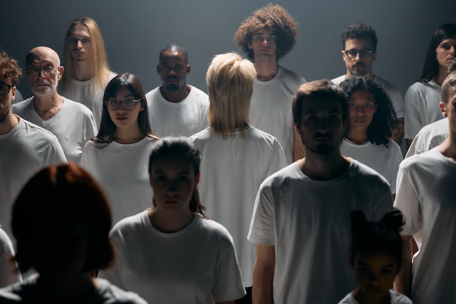 A diverse group of individuals in white shirts standing in a studio setting.