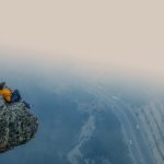 A man in an orange shirt sits on a rocky cliff edge overlooking a foggy road in Mersin, Turkey.
