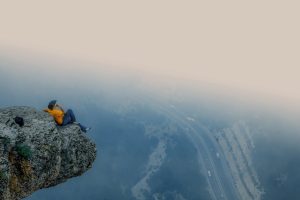 A man in an orange shirt sits on a rocky cliff edge overlooking a foggy road in Mersin, Turkey.