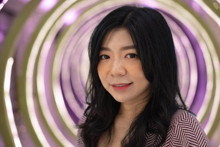 Asian woman with black hair smiling against a neon circular background indoors.