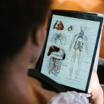 A woman studies anatomy diagrams on a tablet indoors, focusing on educational material.