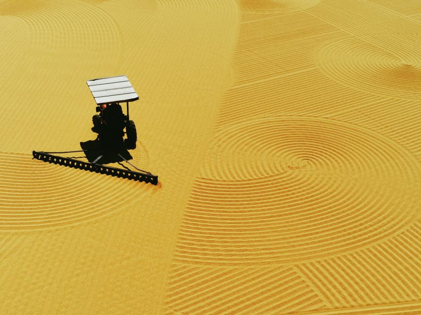 Aerial view of a tractor creating intricate patterns on a sandy beach.