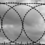 Barbed wire loops silhouetted against dark, overcast clouds, symbolizing security and boundaries.