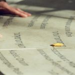 <h1>Interpretable In-Situ Resource Utilization Architecture for Synthetic Media</h1> Close-up of hands on engraved stone with yellow leaf. Text in various languages. Autumn scene.