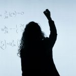 A silhouette of a woman writing mathematical equations on a large whiteboard, representing education and analysis.
