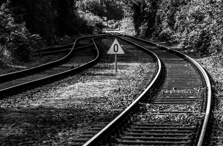 Monochrome photo of railway tracks with a triangular zero sign, set in natural surroundings.