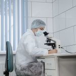 Low-Latency Bioelectronic Medicine for Real-Time AI Scientist in protective gear examining samples under a microscope in a lab.