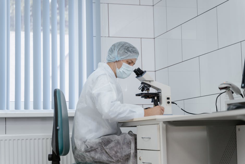 Scientist in protective gear examining samples under a microscope in a lab.