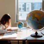 Meta-Learning and GEOINT: Next-Gen Cyber Threat Defense A young girl diligently studying in a sunlit classroom with a globe and books.
