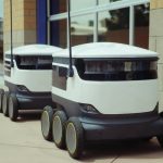 Meta-Learning Logistics Compilers for Cybersecurity Two autonomous delivery robots positioned outside a modern building, showcasing innovation in robotics and mobility.