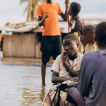 Children in rural village navigate flood waters, depicting resilience.