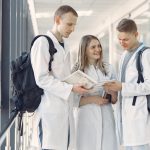 A group of medical students in white coats studying together in a hospital hallway.