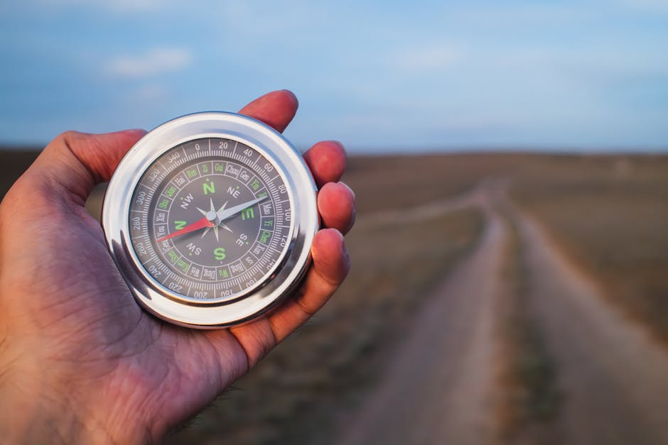 Close-up of a hand holding a compass against a rural path, symbolizing exploration.
