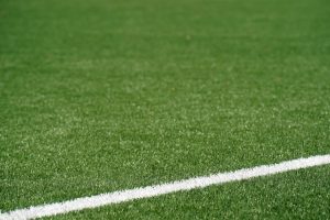 Close-up view of a green artificial soccer field with a white boundary line and space for text.