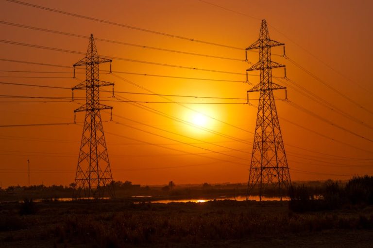 Silhouetted transmission towers under a vibrant sunset in Baghdad, Iraq.