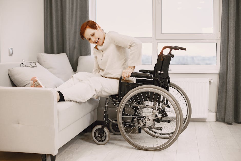 A woman with dyed short hair smiles while transitioning from a wheelchair to a couch.
