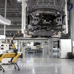A robotic dog oversees an automated car assembly in a high-tech factory setting.