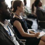 Physics-Informed Intent-Centric Networking for Biotech Data A diverse group of professionals attentively listening at a conference seminar.