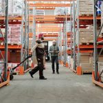 Two workers manage inventory in a spacious warehouse aisle.