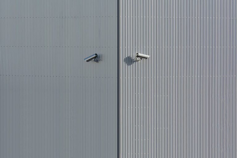 Corrugated metal wall with two mounted security cameras in a minimalist style.