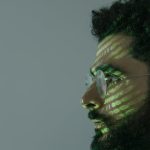 Side profile of a man with eyeglasses and green binary code projected on face.