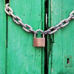 A rustic green wooden door secured with a heavy chain and padlock, symbolizing security.