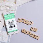 A smartphone showing a COVID-19 health passport next to Scrabble letters spelling 'Ready to Travel'.