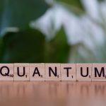 Creative depiction of 'quantum' using wooden letter blocks on a blurred natural background.
