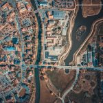 <h1>Risk-Sensitive Geo-Spatial Intelligence Simulators: Engineering Resilient Urban Systems</h1> Aerial shot capturing the intricate city layout with roads, buildings, and a body of water.