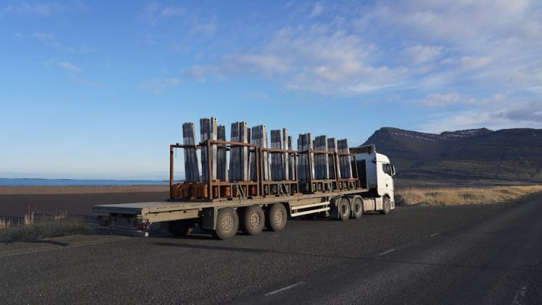 A truck carrying metal cargo on a scenic Icelandic road with mountains in the backdrop.