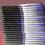 Close-up of stacked metallic sheets reflecting purple light against a gradient background.
