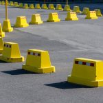 A row of bright yellow traffic barricades on a sunny asphalt road.