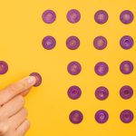 Close-up of a hand arranging purple tokens in a pattern on a vibrant yellow background.
