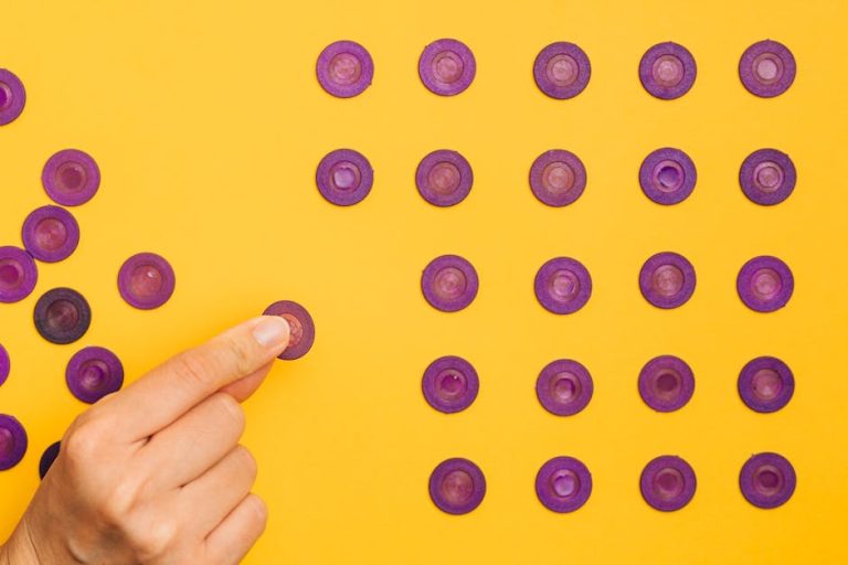 Close-up of a hand arranging purple tokens in a pattern on a vibrant yellow background.