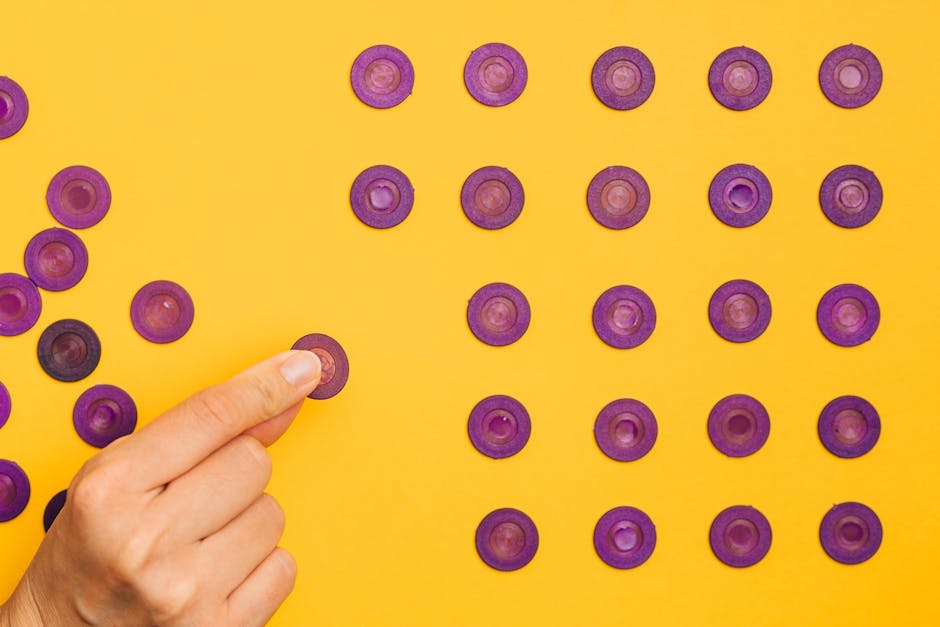 Close-up of a hand arranging purple tokens in a pattern on a vibrant yellow background.