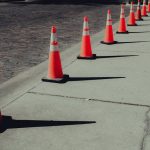A row of bright orange traffic cones on sunlit pavement casting long shadows.