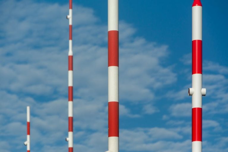 Vertical red and white striped poles extending into the blue sky, conveying height and structure.