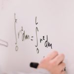 Person writing math equations on a whiteboard, focusing on integrals and formulas.