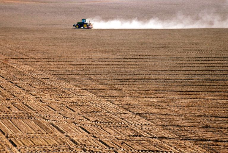 A tractor plowing through a vast, freshly tilled agricultural field during the day.