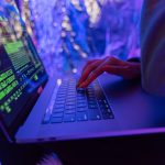 Securing Intelligence With RDS-SMPC Frameworks Close-up of hands typing on a laptop displaying cybersecurity graphics, illuminated by purple light.