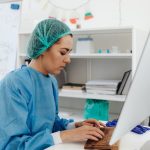 A female healthcare professional in scrub suit working on a computer in a laboratory setting.